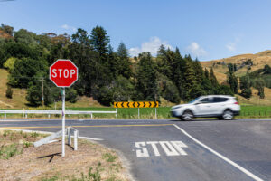 A car passing a road intersection and stop sign, Eskdale, Hastings District, Hawke’s Bay, New Zealand - SCP Stock