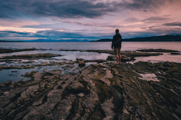 A man standing on Lake Taupo’s foreshore at sunset, Taupo, Waikato, New Zealand - SCP Stock