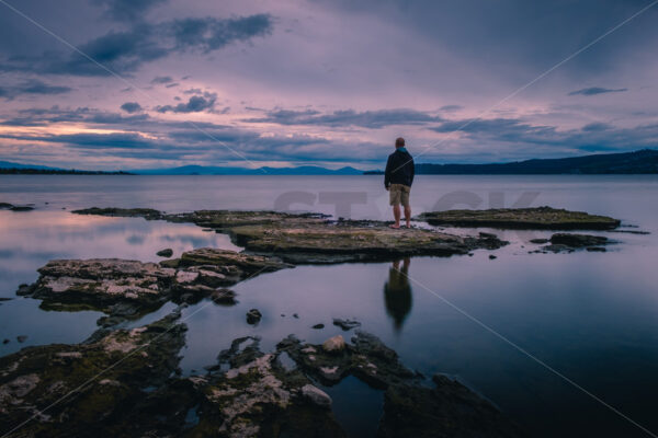 A man standing on Lake Taupo’s foreshore at sunset, Taupo, Waikato, New Zealand - SCP Stock