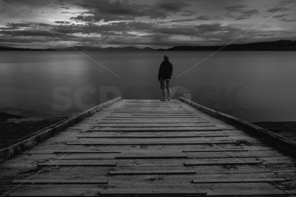 A man standing on a Lake Taupo boat launch ramp at sunset, Taupo, Waikato, New Zealand (black & white) - SCP Stock