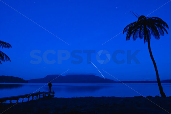 Rocket Man – A man standing on a Lake Tarawera jetty at night watching a Rocket Lab launch, Rotorua, Bay of Plenty, New Zealand (composite image) - SCP Stock